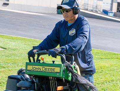 Worker Wearing Headphones Cutting Grass In Summer With A Lawn Mower
