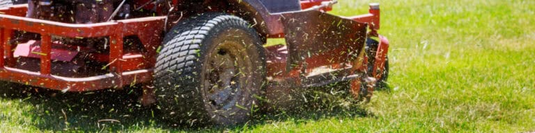 Close up picture of orange riding mower cutting grass.